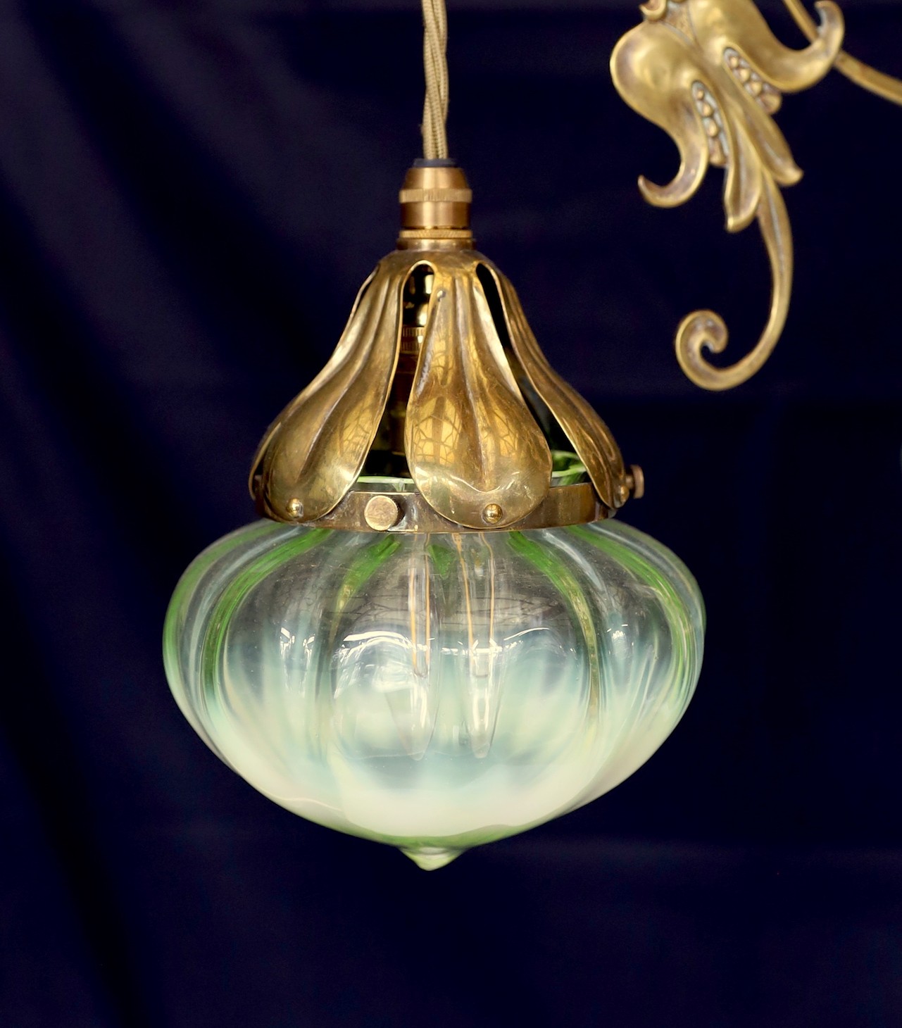 An English Arts & Crafts brass light fitting with scrolling foliate branches and tinted iridescent glass shades, height 68cm. width 46cm